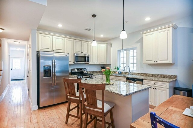 kitchen with appliances with stainless steel finishes, healthy amount of natural light, light wood-style floors, light stone counters, and recessed lighting