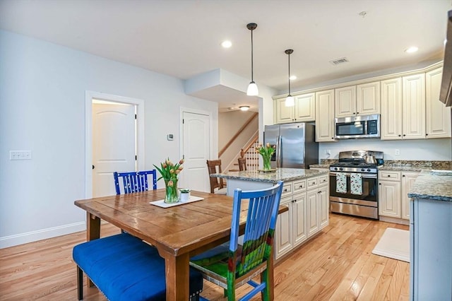 kitchen featuring appliances with stainless steel finishes, light wood-type flooring, a kitchen island, light stone countertops, and baseboards