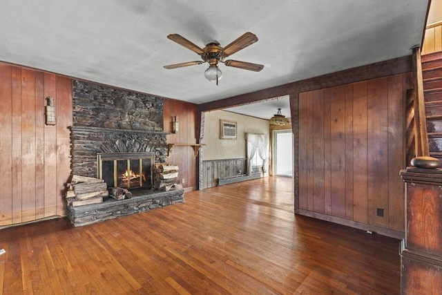 unfurnished living room with ceiling fan, a baseboard heating unit, a fireplace, an AC wall unit, and wooden walls