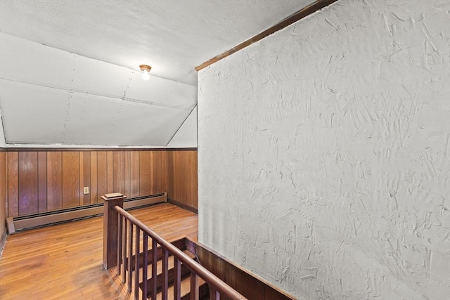 additional living space with light wood-type flooring, wooden walls, and a baseboard radiator