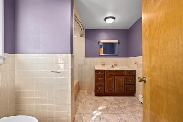 bathroom featuring a shower, tile walls, baseboard heating, vanity, and tile patterned flooring