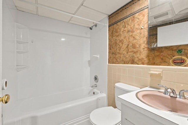 full bathroom featuring washtub / shower combination, toilet, tile walls, vanity, and a drop ceiling