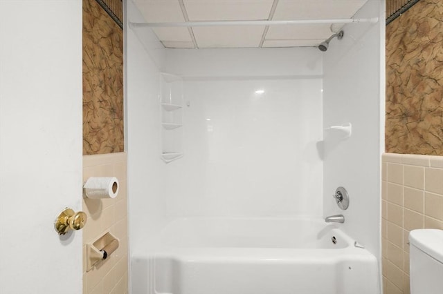 bathroom with toilet, shower / bath combination, and tile walls