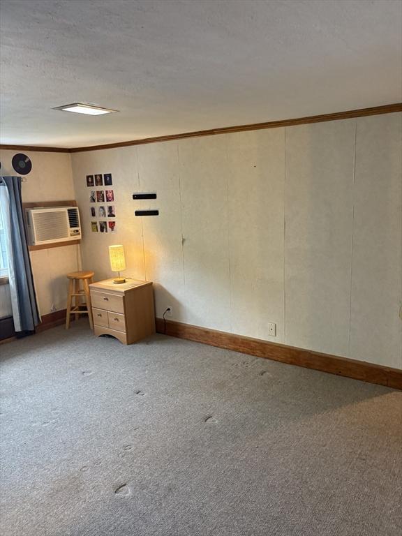 carpeted empty room with crown molding, a textured ceiling, baseboards, and a wall unit AC