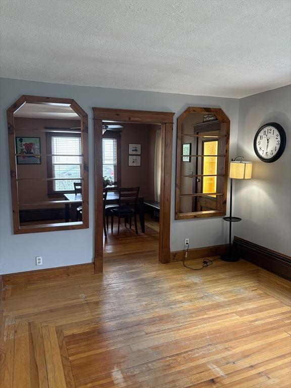 spare room with baseboards, light wood-style flooring, arched walkways, and a textured ceiling