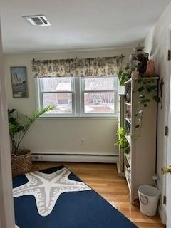 living area featuring baseboard heating, wood finished floors, visible vents, and a healthy amount of sunlight