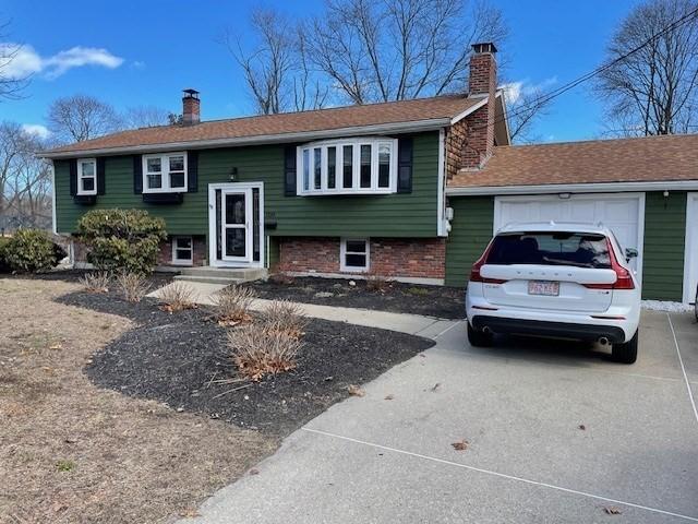 bi-level home featuring driveway, brick siding, a chimney, and an attached garage