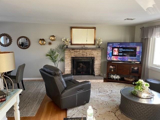 living room featuring visible vents, a fireplace, baseboards, and wood finished floors