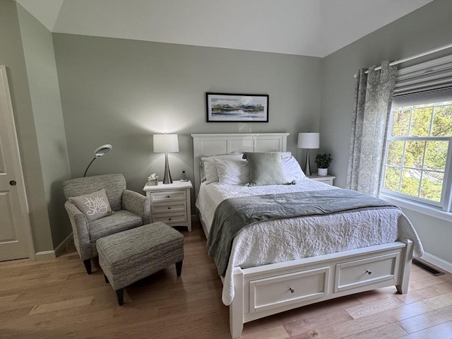 bedroom with multiple windows, light wood-style flooring, baseboards, and lofted ceiling