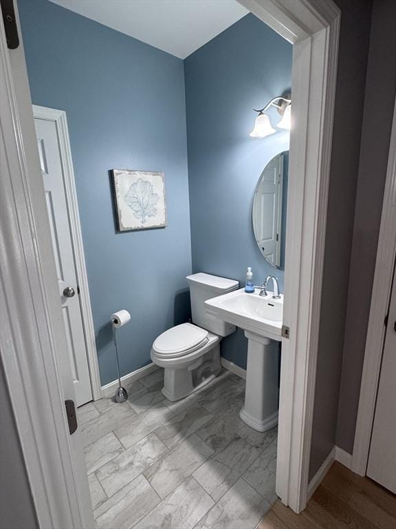 bathroom featuring baseboards, toilet, and marble look tiles