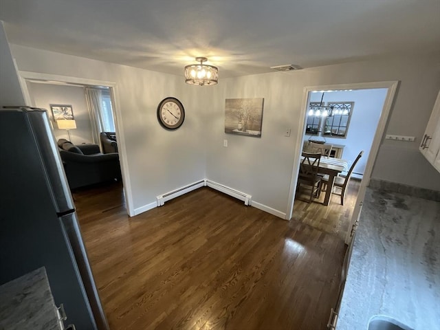 unfurnished dining area featuring baseboard heating, dark hardwood / wood-style flooring, and an inviting chandelier