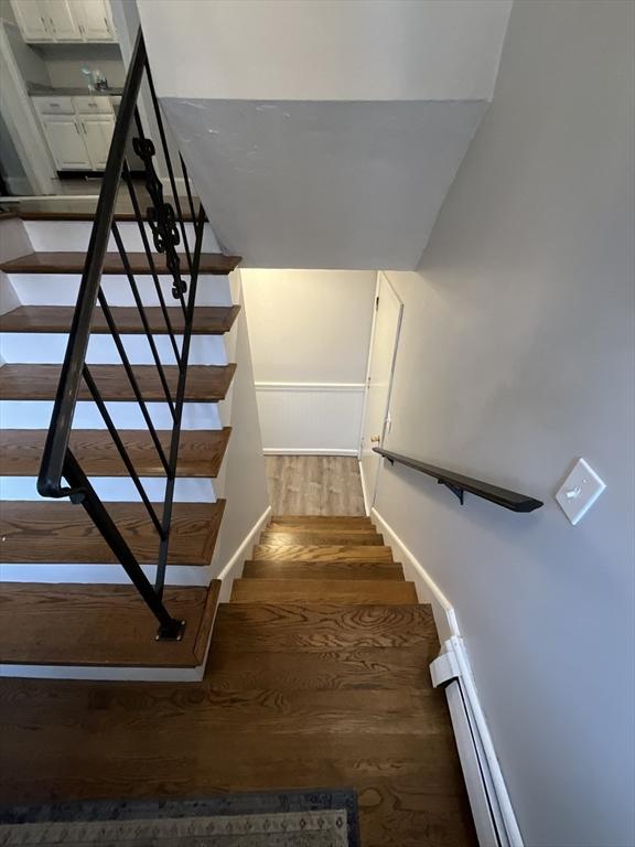 stairs featuring wood-type flooring and a baseboard heating unit