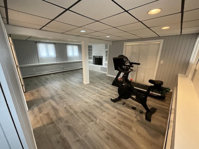 exercise room featuring wood walls, baseboard heating, a drop ceiling, and wood-type flooring