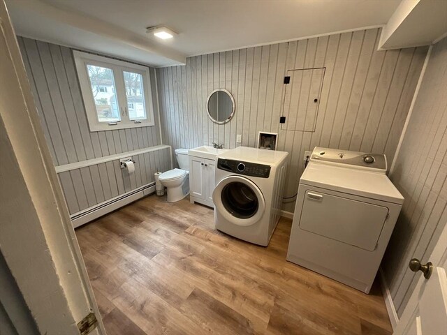 laundry room featuring wood walls, separate washer and dryer, light hardwood / wood-style flooring, and a baseboard radiator