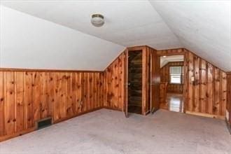 bonus room featuring light carpet, vaulted ceiling, and wood walls