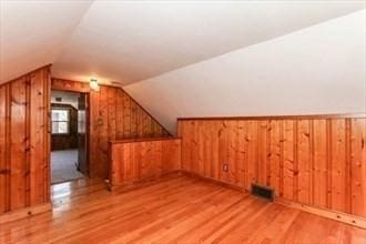 bonus room with wood walls, lofted ceiling, and light hardwood / wood-style flooring