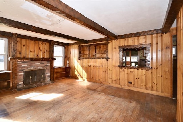 unfurnished living room featuring a brick fireplace, beamed ceiling, wooden walls, and wood-type flooring