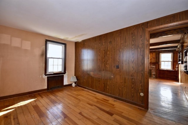 empty room featuring baseboards, wood-type flooring, radiator, and wood walls