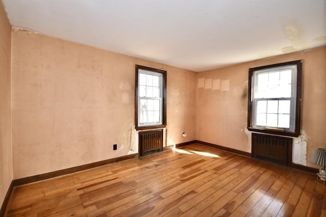 empty room featuring radiator heating unit, baseboards, and wood-type flooring