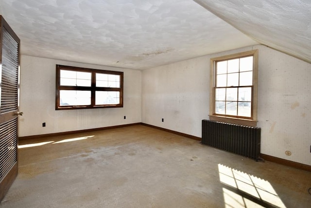 carpeted spare room with plenty of natural light, radiator, baseboards, and vaulted ceiling