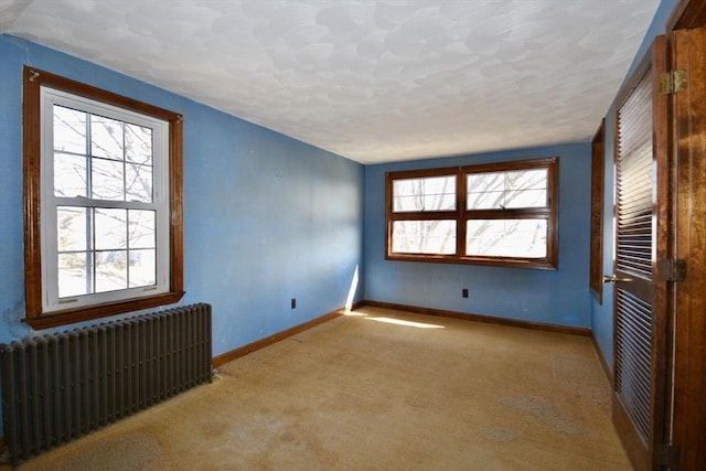 empty room featuring baseboards, radiator, and carpet flooring