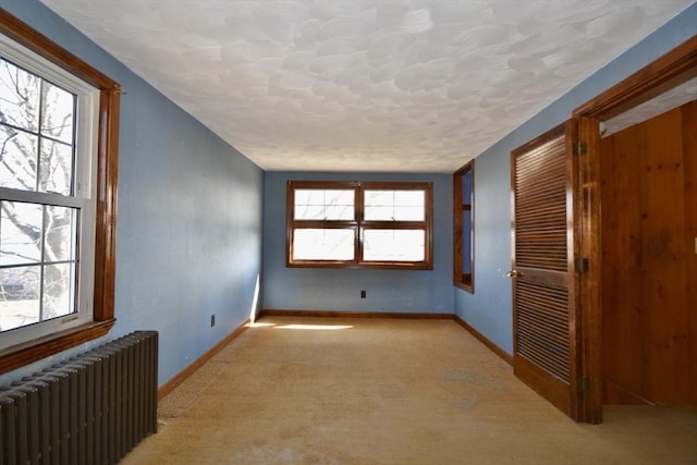 unfurnished room with radiator heating unit, light colored carpet, and baseboards