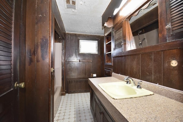 bathroom featuring a textured ceiling, radiator, wood walls, bathtub / shower combination, and vanity