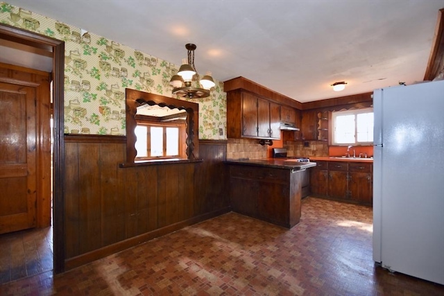 kitchen with wallpapered walls, under cabinet range hood, wainscoting, a peninsula, and freestanding refrigerator