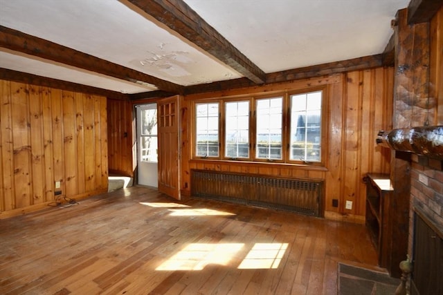 unfurnished living room with wooden walls, baseboards, radiator heating unit, wood-type flooring, and beamed ceiling