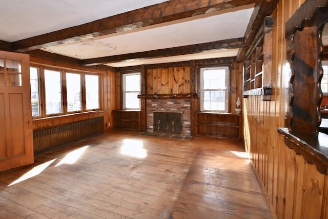 unfurnished living room featuring wooden walls, beamed ceiling, radiator, and hardwood / wood-style flooring