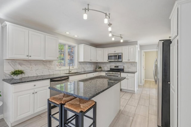 kitchen with sink, appliances with stainless steel finishes, dark stone countertops, white cabinets, and a kitchen island