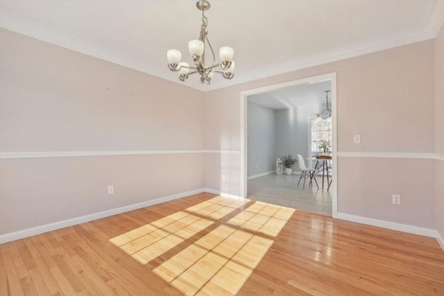 spare room with an inviting chandelier, ornamental molding, and hardwood / wood-style floors