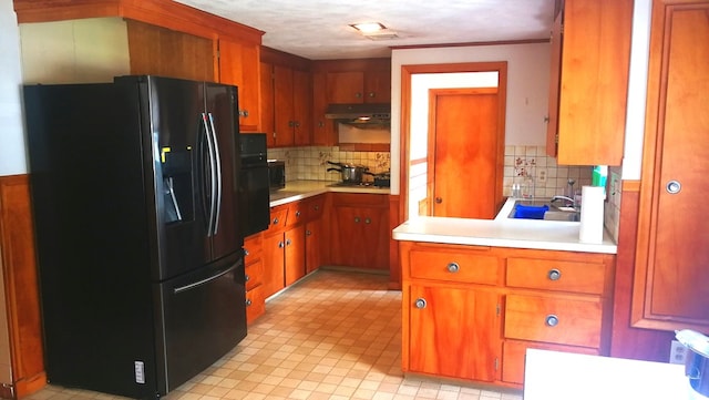 kitchen featuring black appliances, under cabinet range hood, light countertops, and brown cabinetry