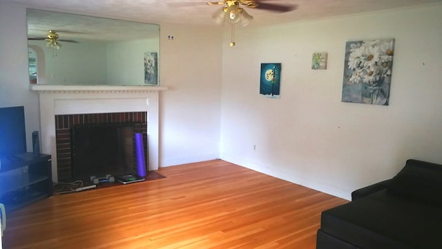 living area featuring ceiling fan, a fireplace, and wood finished floors