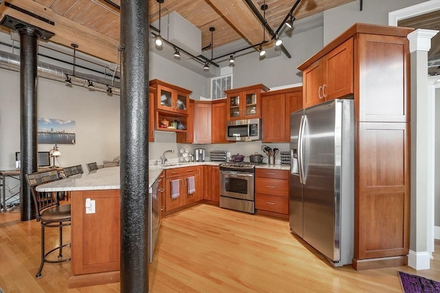 kitchen featuring a kitchen breakfast bar, light stone counters, stainless steel appliances, sink, and light hardwood / wood-style flooring