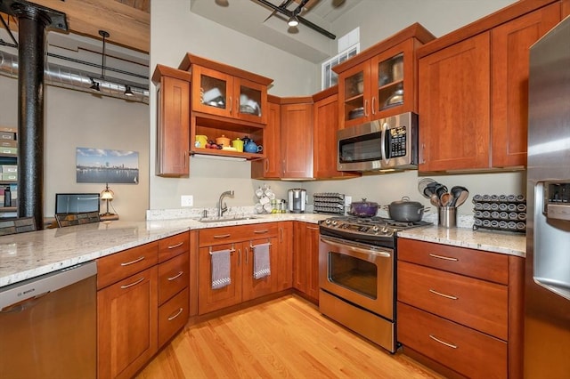 kitchen featuring appliances with stainless steel finishes, light stone counters, light hardwood / wood-style flooring, and sink