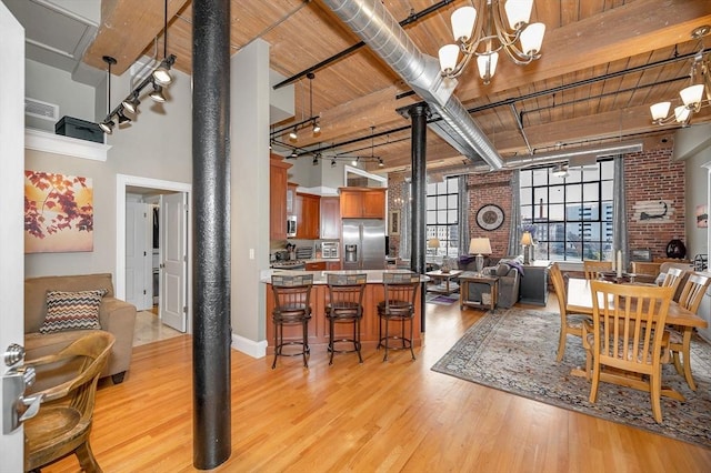 dining room featuring wooden ceiling, light hardwood / wood-style flooring, a towering ceiling, brick wall, and a chandelier