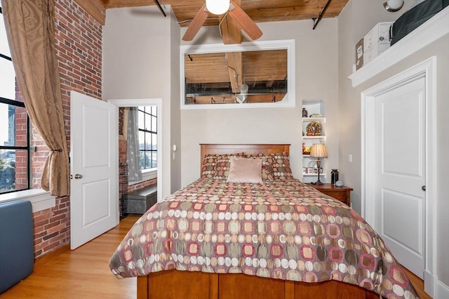 bedroom featuring wooden ceiling, ceiling fan, beamed ceiling, light hardwood / wood-style floors, and brick wall