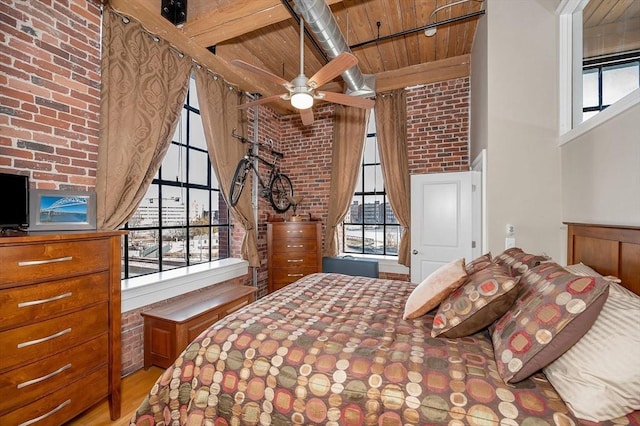 bedroom featuring ceiling fan, light hardwood / wood-style flooring, brick wall, and multiple windows