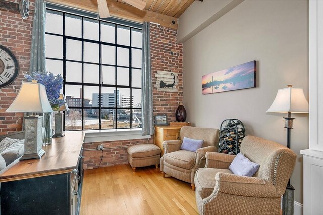 living area featuring brick wall, beam ceiling, light wood-type flooring, and wood ceiling