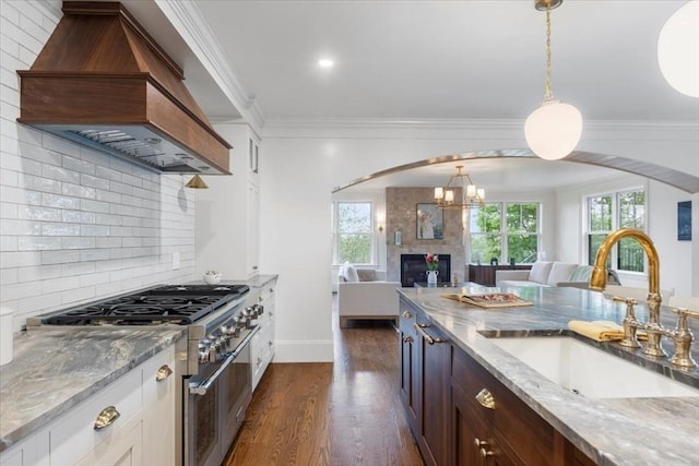 kitchen featuring stainless steel range, premium range hood, a sink, open floor plan, and dark wood-type flooring