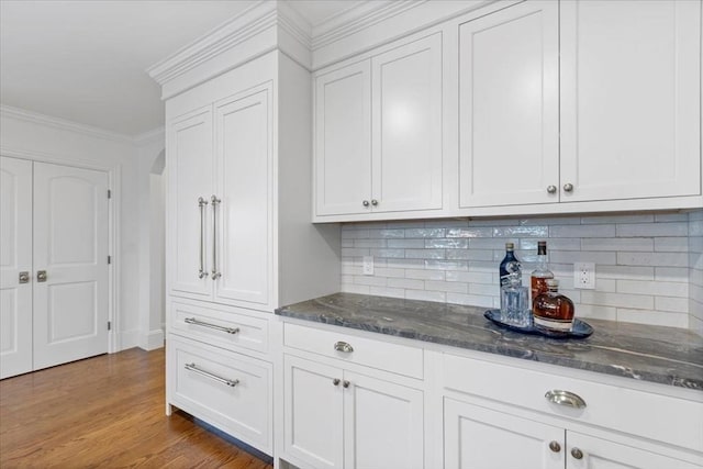 kitchen featuring backsplash, dark stone countertops, white cabinets, and ornamental molding