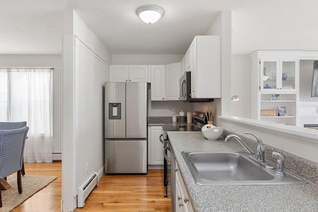 kitchen with a sink, white cabinets, appliances with stainless steel finishes, baseboard heating, and glass insert cabinets