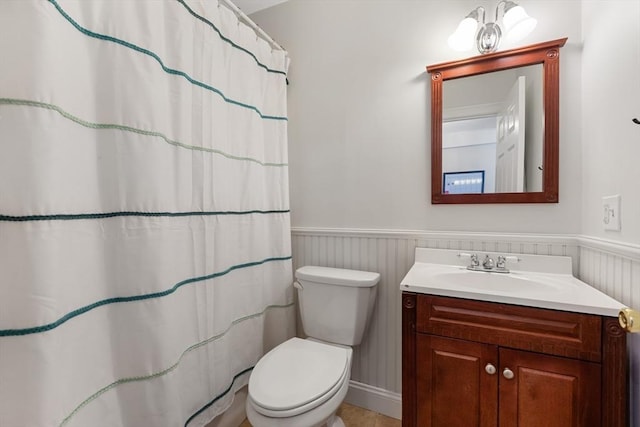 bathroom featuring curtained shower, a wainscoted wall, vanity, and toilet