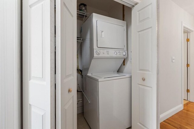 laundry room featuring light wood-style floors, stacked washer / dryer, laundry area, and baseboards