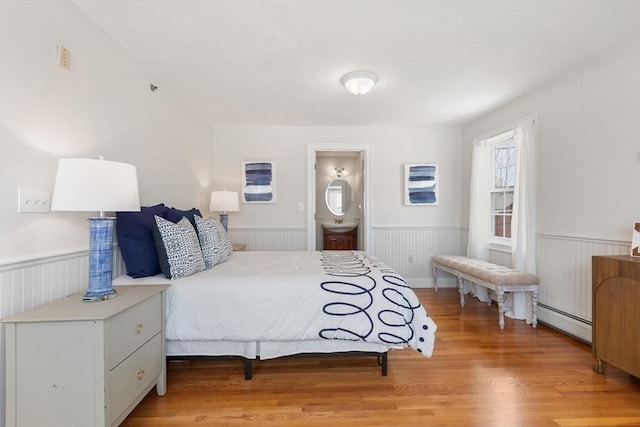 bedroom with light wood-type flooring, baseboard heating, and wainscoting