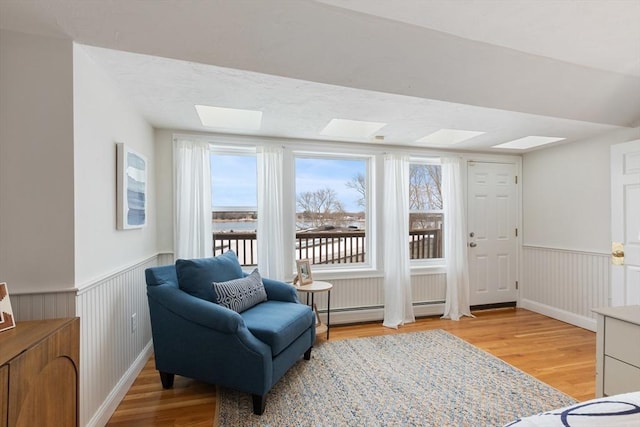 sitting room with a wainscoted wall, a skylight, baseboard heating, and wood finished floors