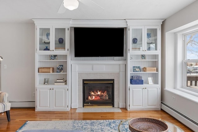 living room with a baseboard heating unit, a tile fireplace, and light wood finished floors