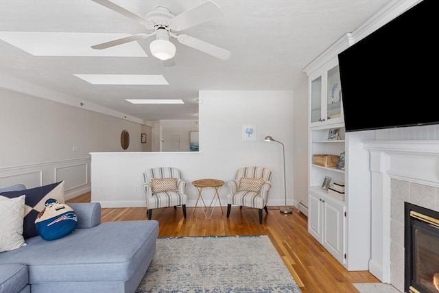 living area featuring a baseboard heating unit, light wood-type flooring, ceiling fan, and a tiled fireplace