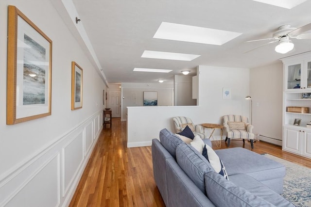 living area featuring light wood-style floors, baseboard heating, a skylight, and a decorative wall